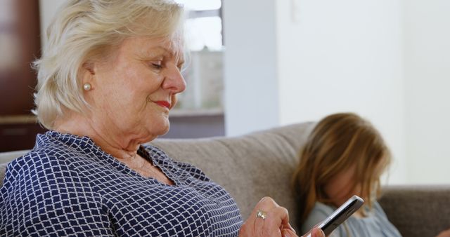 Elderly woman using smartphone with granddaughter playing in background - Download Free Stock Images Pikwizard.com