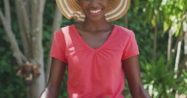 Happy african american woman wearing pin t-shirt and hat, smiling in garden. Lifestyle and domestic life.