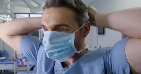 Surgeon Securing Surgical Mask and Preparing for Procedure Under Operating Light