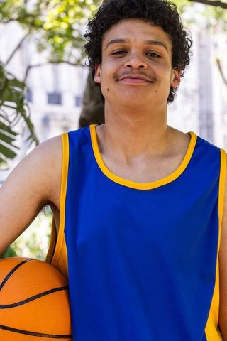 Confident african american basketball player wearing blue jersey holding ball in park