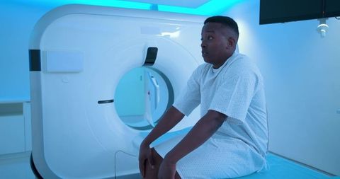 Male patient sitting on ct scanner table wearing hospital gown waiting for radiology scan