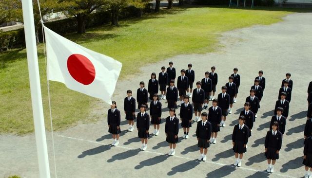 Students standing in formation during flag-raising at japanese schoolyard