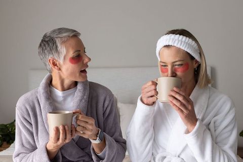 Two women enjoying morning skincare ritual with under-eye patches, bathrobes and coffee