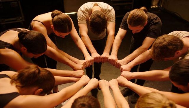 Ensemble forming circle and joining fists before performance, conveying unity and focus