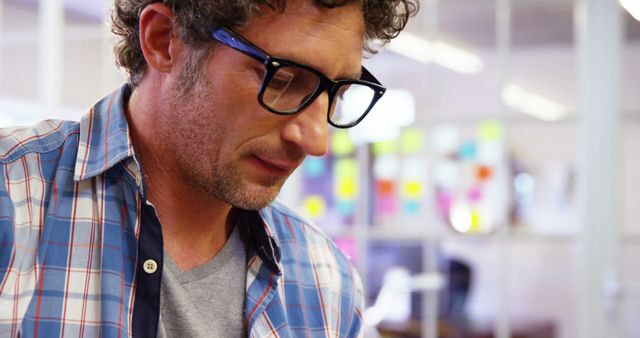 Man in glasses engaging in work at modern office space, useful for depictions of professional environments, creative processes, and modern work culture.