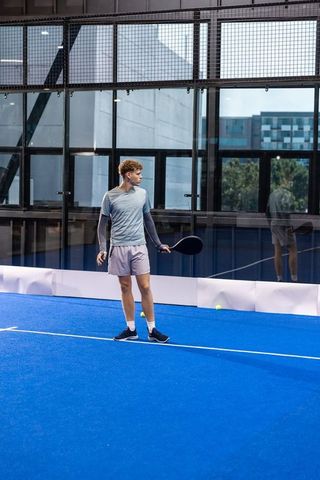 Young athlete standing on blue padel court holding racket, preparing to play