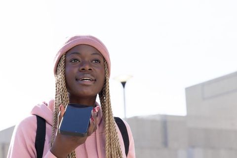 Teen african american student speaking into phone outdoors wearing pink beanie and hoodie
