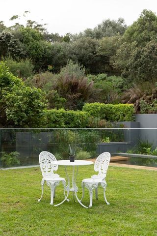 White ornate bistro set sitting on manicured lawn with potted succulent and glass balustrade