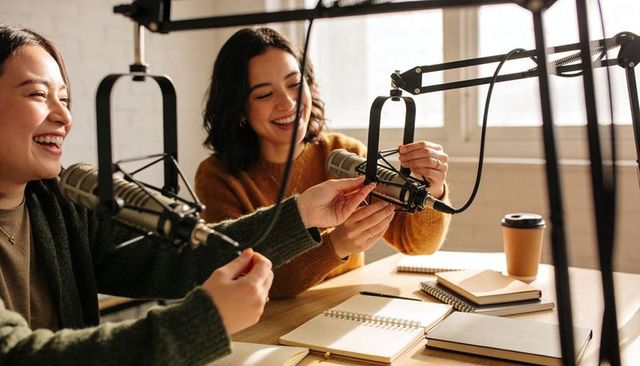 Two Podcast Hosts Adjusting Broadcast Microphones in Bright Collaborative Studio, Smiling