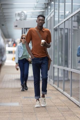 Urban commuter walking with coffee and crossbody satchel on glass transit platform