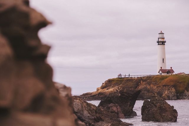 Lighthouse standing tall on rocky coastal terrain with cloudy sky, capturing a maritime scene. This image is ideal for travel blogs, tourism advertisements, or websites focusing on coastal adventures and maritime history.
