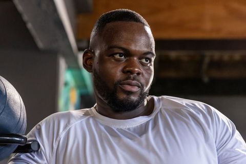 Focused african american man resting between sets on gym bench for strength training