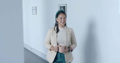 Stylish Professional Woman Holding Coffee Mug in Office Hallway