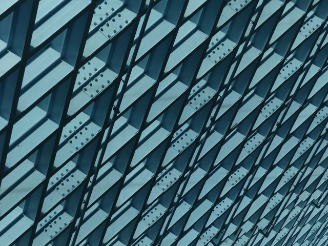 Close-up view of a modern building facade with a unique geometric pattern. Suitable for use in architecture magazines, urban design blogs, and construction industry advertisements. Highlights innovative structure designs and contemporary architectural trends.