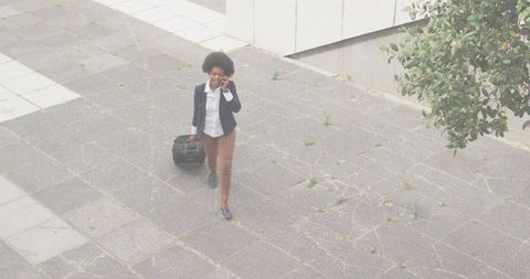 Confident businesswoman talking on smartphone while pulling briefcase