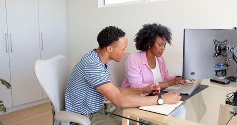 Joyful couple collaborating at home desk on laptop