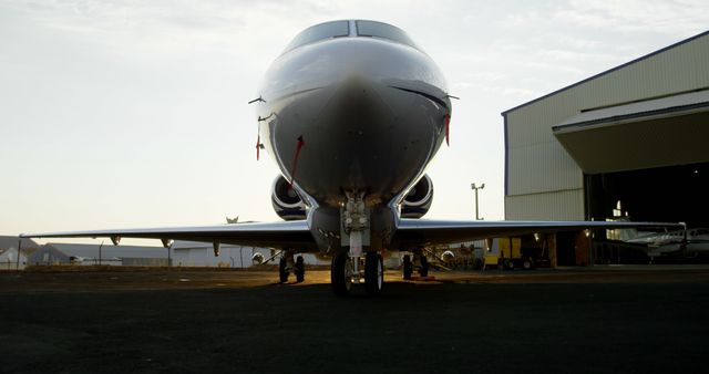 The image depicts a modern private jet parked just outside a hangar, highlighting its sleek front profile and jet engines. This can be used for representations related to aviation, luxury travel, and business aviation. Ideal for website headers, travel blogs, aviation magazines, and marketing materials for private jet services.