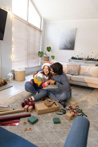 Couple wrapping christmas gifts at home in cozy living room, romantic holiday moment