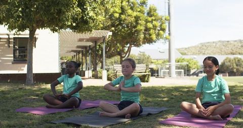 Multicultural girls practicing outdoor yoga on mats in schoolyard mindfulness class