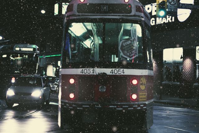 Streetcar moving through a snowy night city street with traffic, showcasing winter conditions and urban transportation. Ideal for themes involving night scenes, public transport, city life, cold weather, and wintertime challenges.
