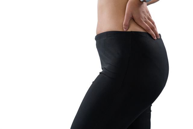 Mid section of female athlete massaging back while standing against white background