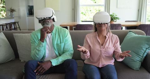 Diverse senior couple exploring virtual reality at home with white vr headsets