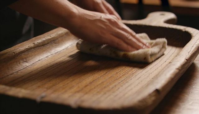 Wiping rustic carved wooden serving board with cloth, kitchen care