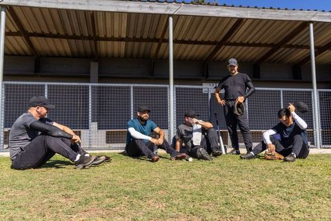 Baseball teammates resting on grass in front of dugout during sunny practice
