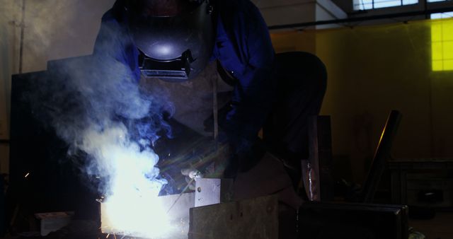 Welder working with protective mask, engulfed in sparks and smoke. Suitable for representing industrial processes, safety in manufacturing, skilled labor, and engineering environments. Useful for articles and content related to welding techniques, occupational safety, and metal fabrication.