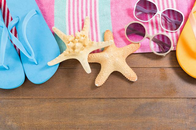 Colorful beach accessories, including blue and orange sandals, pink and green striped towel, sunglasses, and starfish on a wooden board. Ideal for promoting summer vacations, travel destinations, beach resorts, and casual summer wear.