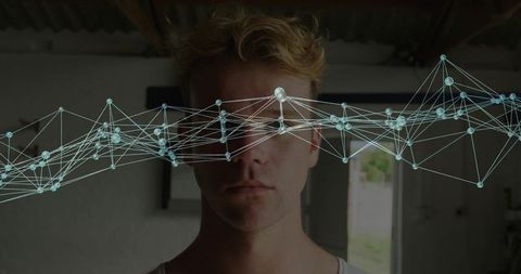 Young man in white tank with glowing network overlay over eyes in moody industrial loft