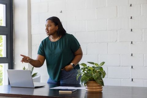 African american woman leaning toward laptop pointing during remote meeting in minimalist workspace