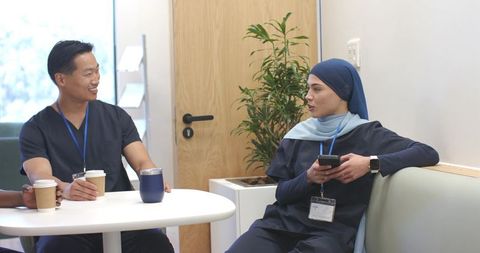Multicultural medical staff in navy scrubs chatting in modern clinic breakroom over coffee midday