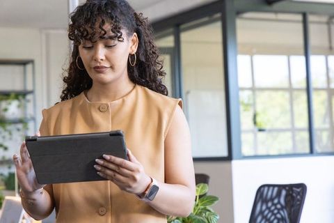 Professional woman using tablet in modern office with smartwatch, glass partitions, plants