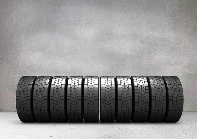 Uniform arrangement of tyres in front of an industrial concrete wall. Perfect for automotive industry promotions, tyre shop advertisements, or illustrating repair services. Can be used on websites, in magazines, or for posters.