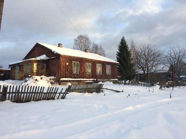 Snow-covered wooden house with trees and a fence in countryside during winter. Great for portraying wintertime rural life, seasonal change, solitude, and natural beauty walks.