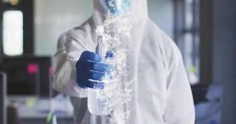 Hazmat technician spraying disinfectant in office wearing nitrile gloves and protective suit