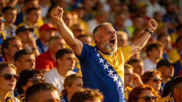 Cheering bearded fan raising arms wearing bosnia and herzegovina jersey in stadium crowd
