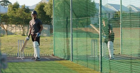 Cricket batsman practicing in net lane wearing helmet and pads at outdoor turf facility