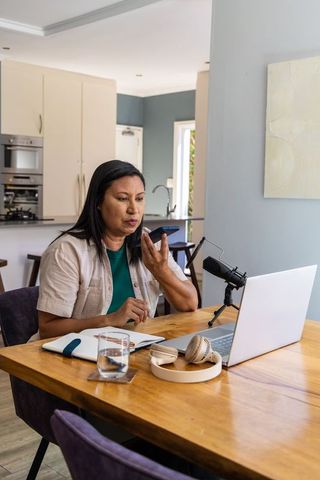 Asian woman recording podcast at home office with laptop microphone and notebook