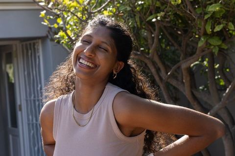 Laughing african american woman in sunny courtyard wearing gold chains and hoops