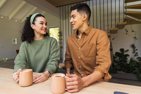Young couple sharing coffee and conversation in modern minimal kitchen with matching mugs