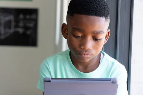 African american boy studying on tablet by window in classroom natural light focused