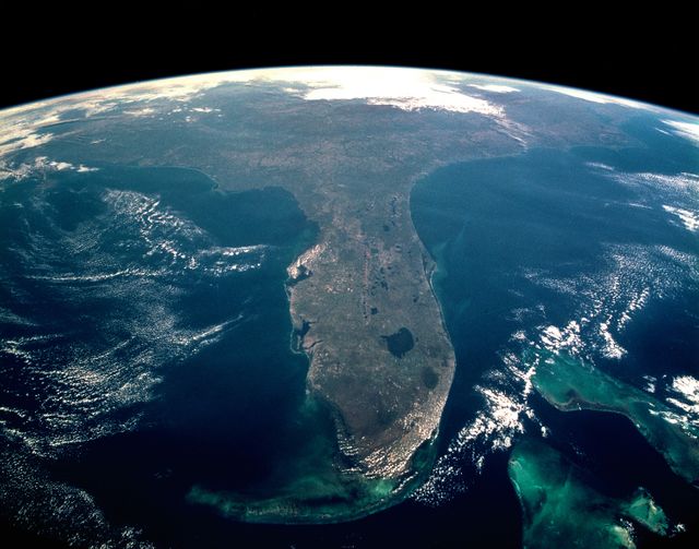 Photograph showing a detailed foreshortened view of Florida Peninsula attached during STS-95 mission by NASA. Key features include Florida Keys, Bahama Banks, 'popcorn' cumulus cloud over Miami, and noticeable Cape Canaveral. Orlando and Lake Okeechobee are also visible. Usable in presentations, educational materials concerning space exploration, weather conditions, geographical surveys or features, and oceanography.