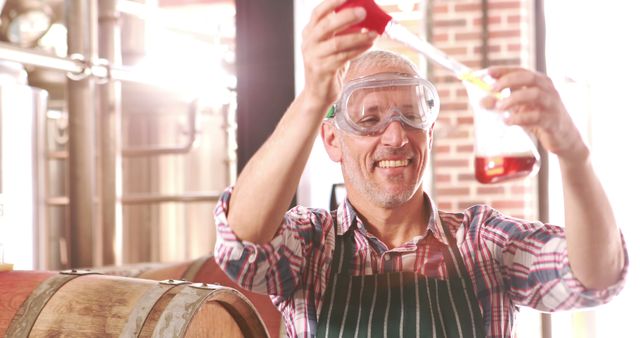 Man smiling while testing beer quality in brewery using laboratory equipment. Wearing goggles and apron, indicating focus on safety and precision. Ideal for articles and advertisements related to brewing, beer quality, and artisanal alcohol production. Also useful for educational content around the science of brewing and small business brewery stories.