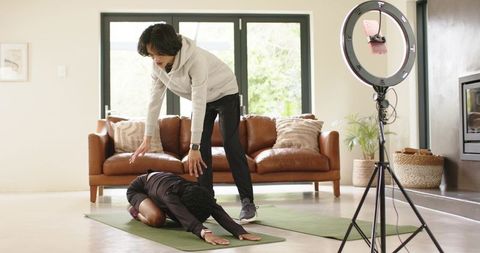 Male coach guiding african american woman through yoga stretch during home livestream