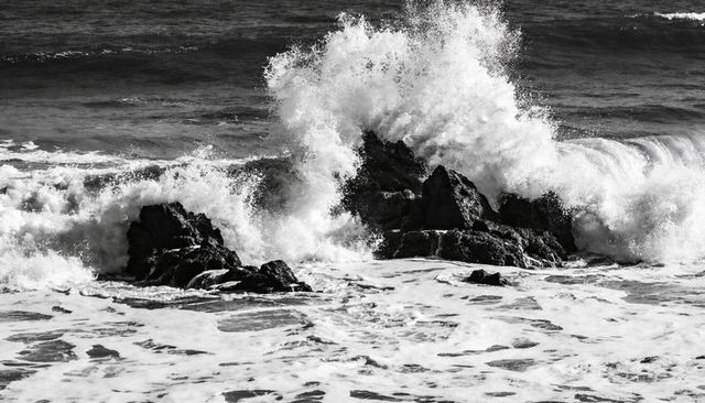 Monochrome waves crashing against jagged coastal rocks with exploding spray and foam