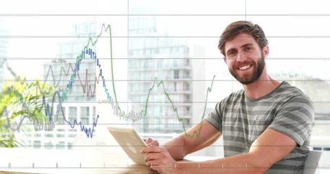 Smiling bearded man holding tablet analyzing financial charts in office with city view