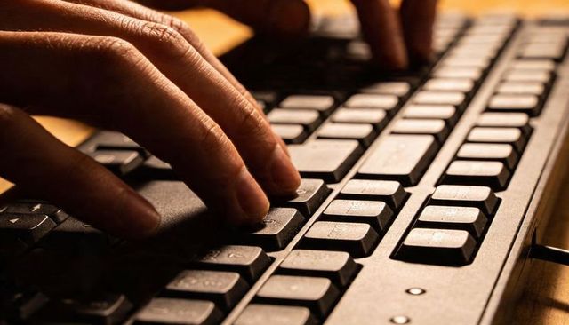 Typing hands pressing keys under warm lamp light on wooden desk closeup texture