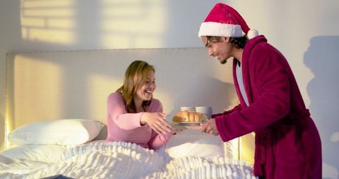 Couple sharing cozy breakfast in bed on holiday morning with man wearing santa hat